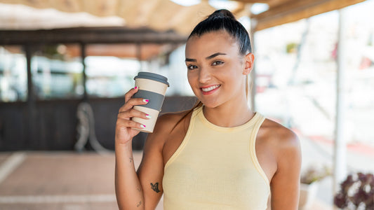 a female athlete holding a cup of coffee with a blurred bokeh outdoor gym in the background